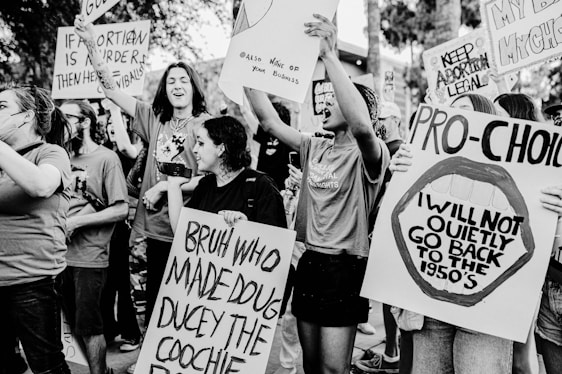 A group of people are actively participating in a protest, holding various signs and banners with slogans related to pro-choice and abortion rights. The scene is dynamic, with individuals expressing strong emotions and displaying a sense of unity and activism.