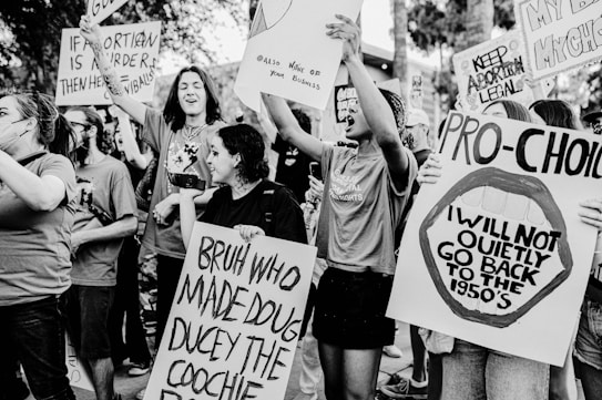 A group of people are actively participating in a protest, holding various signs and banners with slogans related to pro-choice and abortion rights. The scene is dynamic, with individuals expressing strong emotions and displaying a sense of unity and activism.