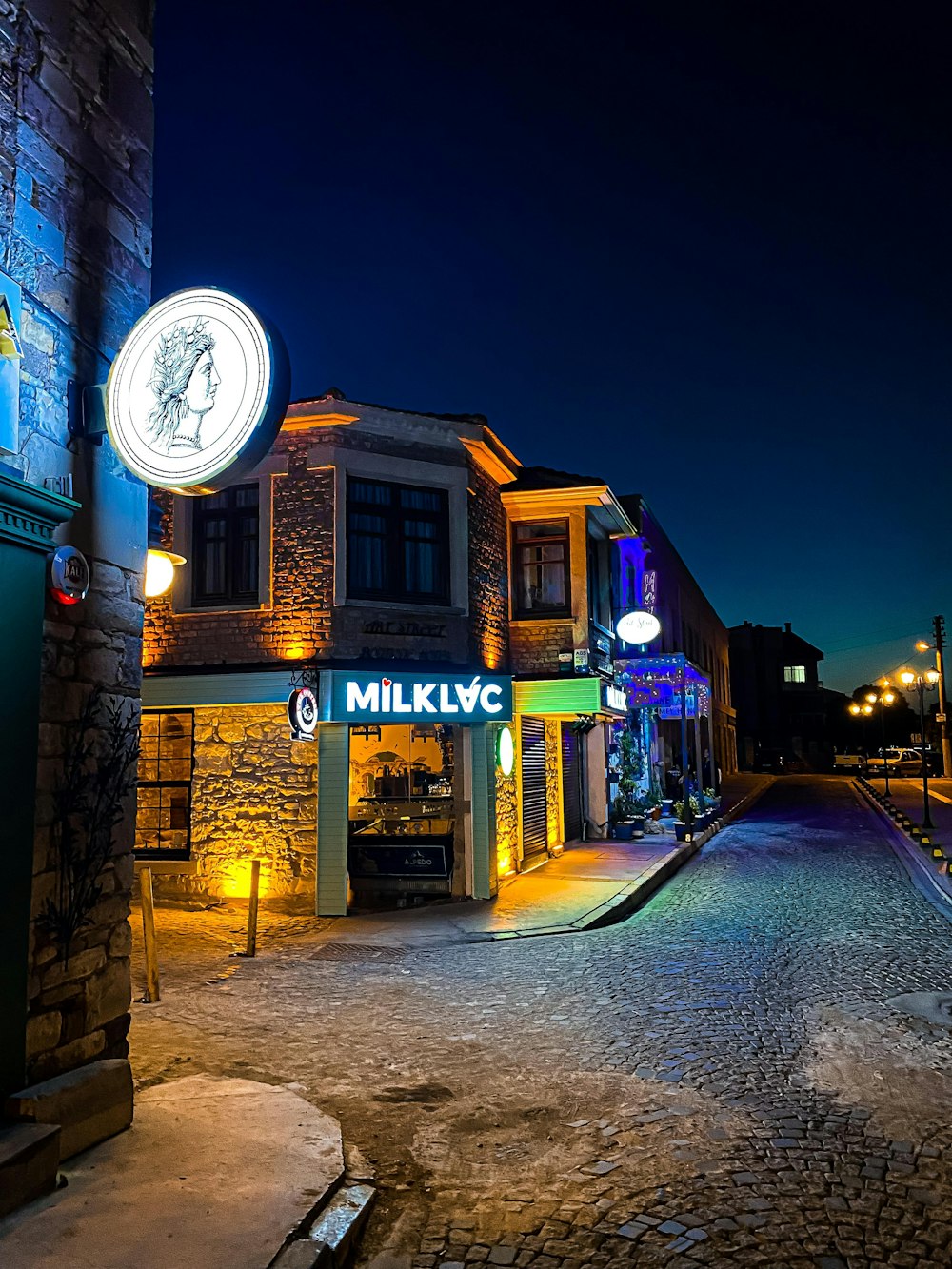 a cobblestone street at night with a neon sign