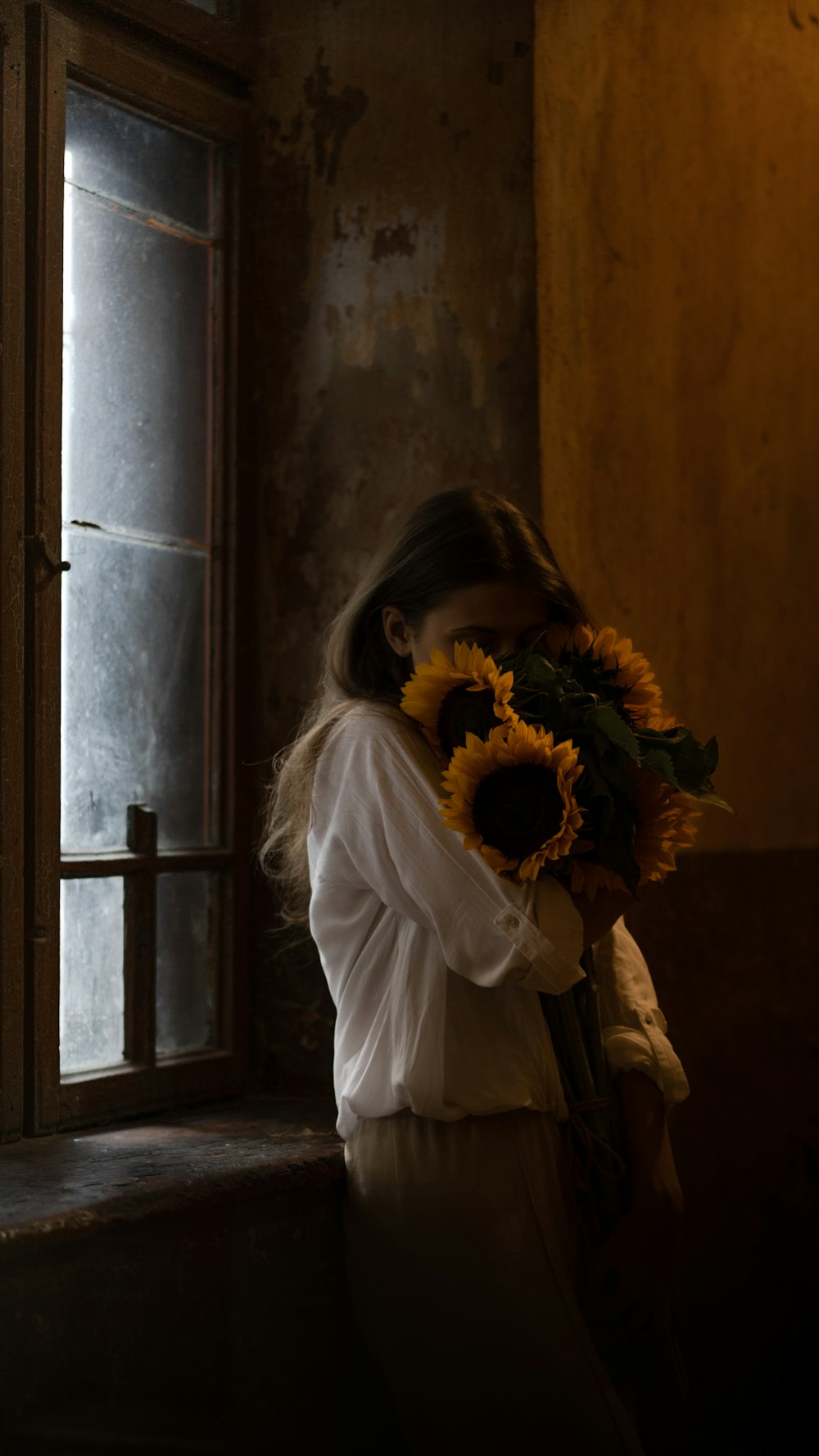 Una mujer sosteniendo un ramo de girasoles frente a una ventana