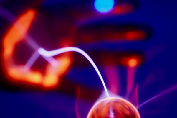 Multi-colored lights, with shades of blue, red, and purple, create a captivating scene featuring a hand and a plasma ball emitting glowing trails in a dark setting.