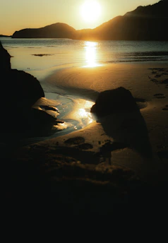 A serene aerial shot of Perth's coastline at golden hour, with soft waves and warm sunlight casting long shadows.