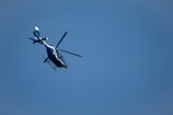 A helicopter with a sleek design is flying against a backdrop of a clear blue sky. It appears to be angled slightly upward as it moves through the air.