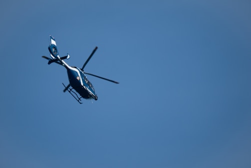 A helicopter with a sleek design is flying against a backdrop of a clear blue sky. It appears to be angled slightly upward as it moves through the air.