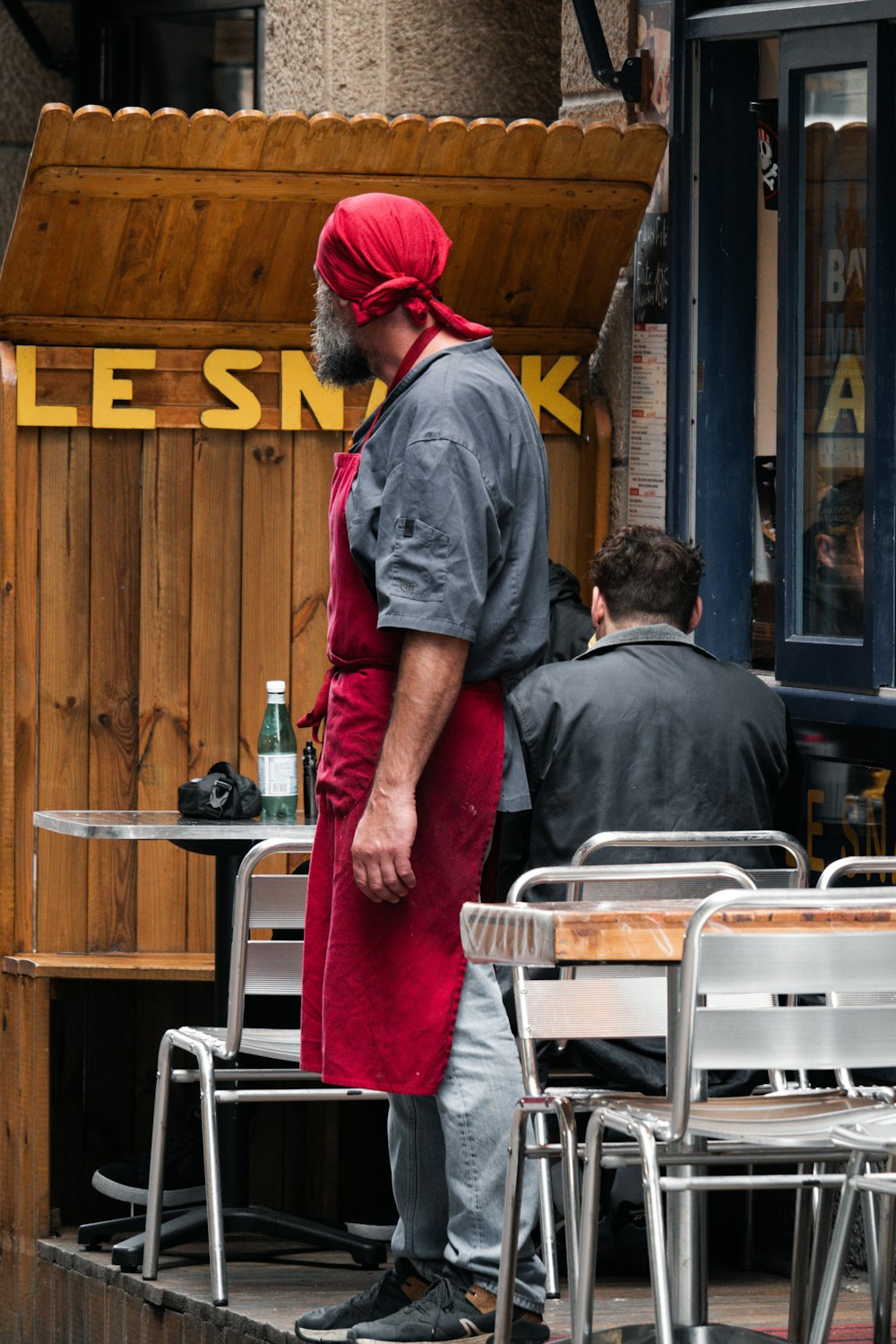 a man in a red apron is standing outside of a restaurant