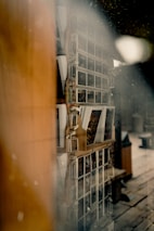 A display rack with multiple rows of postcards is visible through a slightly fogged or dusty glass. The postcards are arranged neatly, with each row containing various images, possibly depicting scenic or artistic photos. There is a warm, wooden frame around the display and the surrounding area hints at a rustic interior setting.