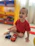 A happy child playing with a bright red juguetiva toy truck on a wooden floor.
