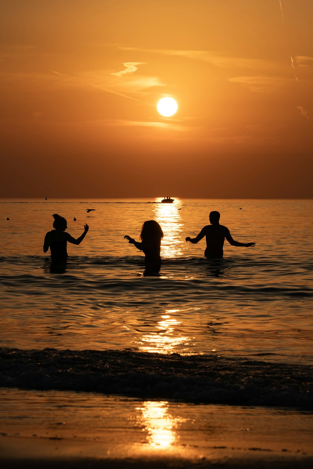 a group of people wading in the ocean at sunset