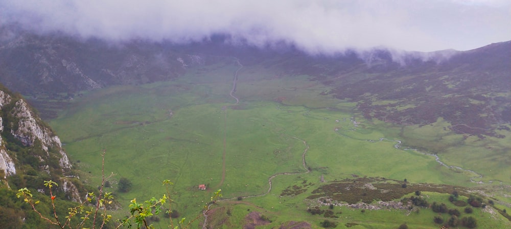 a lush green valley surrounded by mountains under a cloudy sky