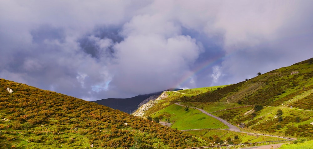 a rainbow in the sky over a lush green hillside