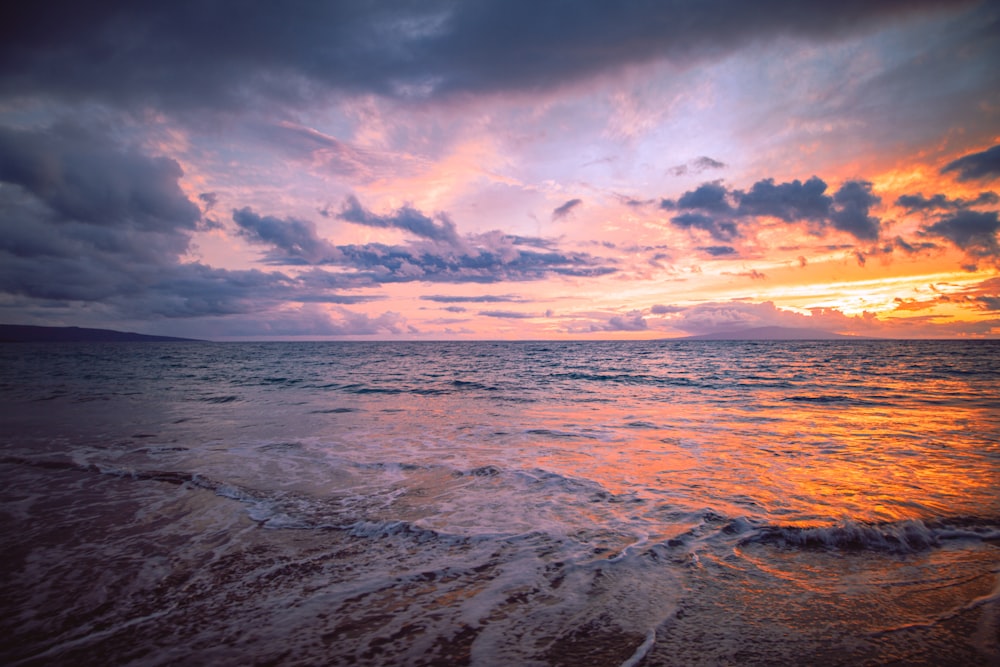 a sunset over the ocean with waves coming in