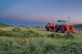 A bright red tractor parked beside a golden wheat field under a clear blue sky.