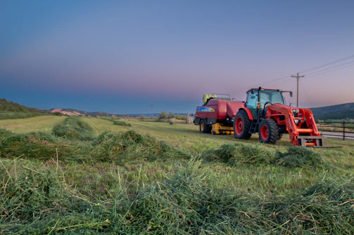A bright red tractor parked beside a golden wheat field under a clear blue sky.
