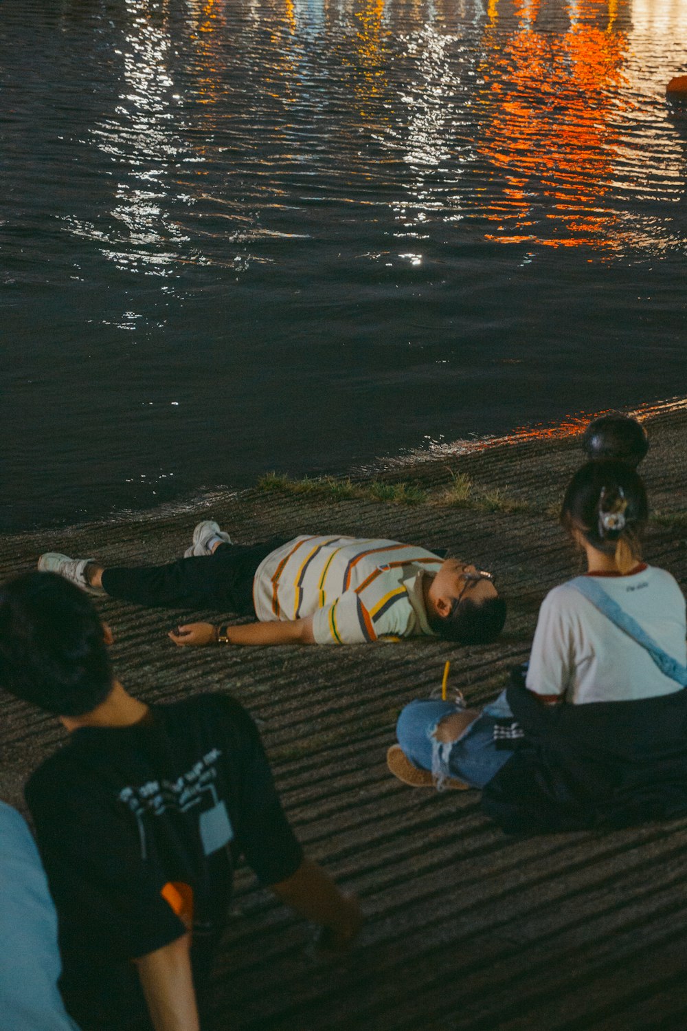 Un grupo de personas sentadas en el suelo junto a un cuerpo de agua