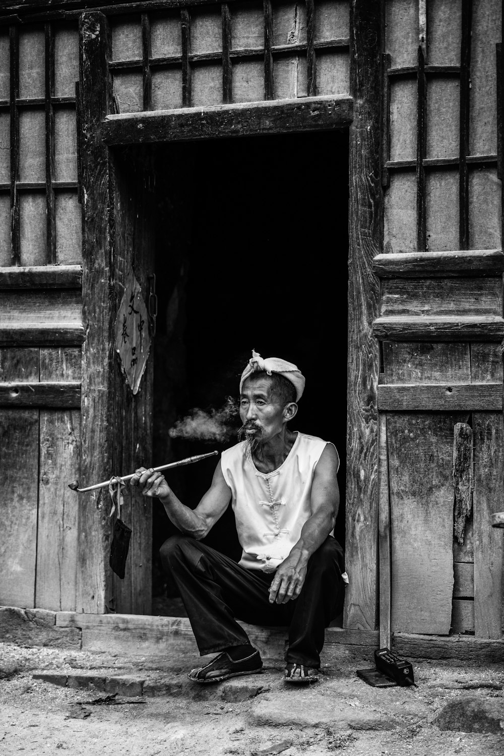 Un hombre sentado en una puerta fumando una pipa