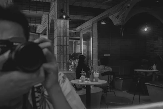 A cozy Scandinavian-style restaurant corner with warm lighting, featuring a team member capturing behind-the-scenes shots on a camera.