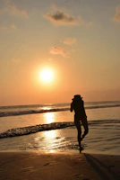 A man wearing a redflip bucket hat standing on a rocky beach during sunset.