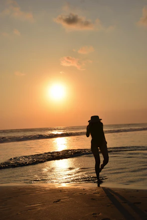 A man wearing a redflip bucket hat standing on a rocky beach during sunset.