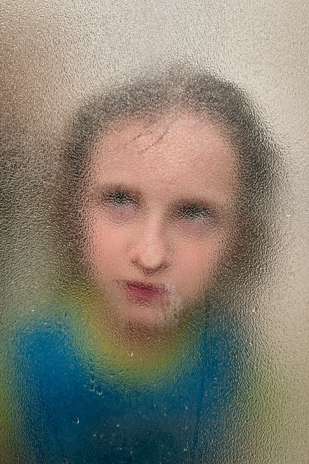 a blurry image of a young girl's face behind a frosted glass