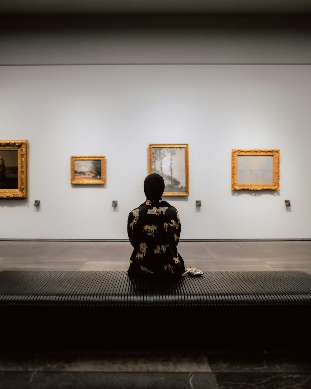 a person sitting on a bench in front of paintings