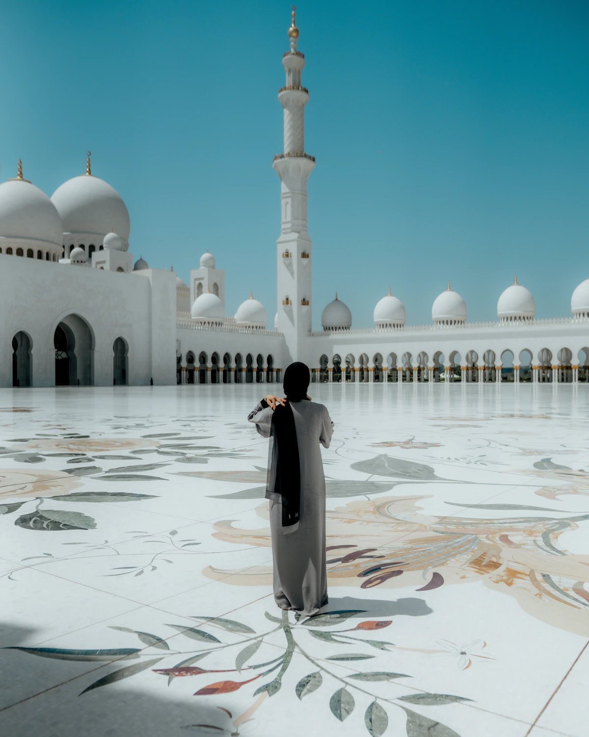 A visitor standing beneath the white domes and arches of Sheikh Zayed Grand Mosque