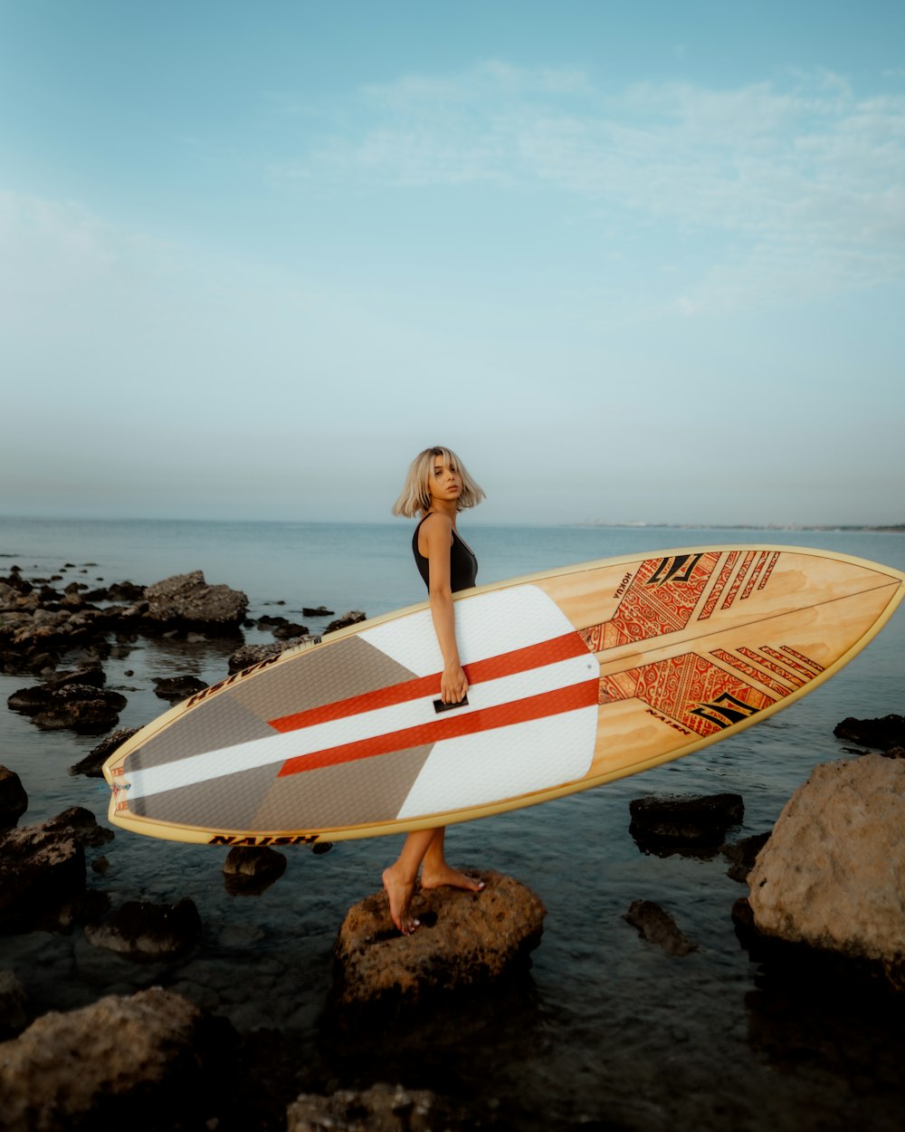 a woman holding a surfboard on top of a rocky beach