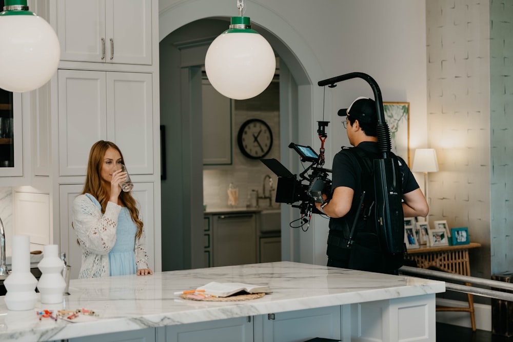 a woman is filming a man in a kitchen