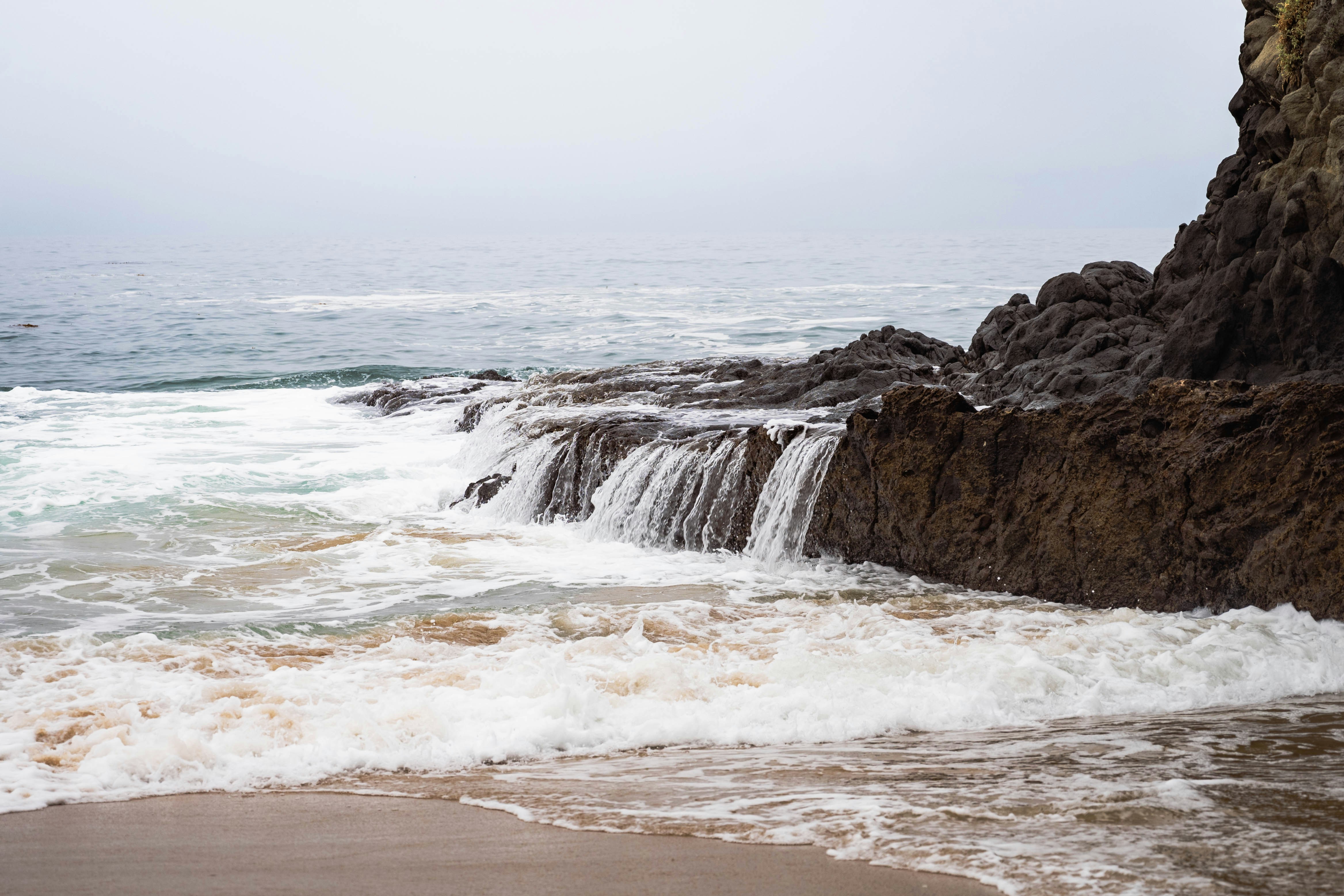 a man standing on a beach next to a waterfall