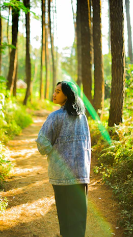 A candid shot of a person walking through a sunlit forest trail, surrounded by tall trees.