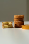 Several slices of cake are arranged on a white surface. On the left, two pieces are stacked with the cake's soft, fluffy interior visible. Toward the right, a stack of four round cakes is neatly aligned, showing their golden-brown crusts.