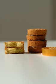 Several slices of cake are arranged on a white surface. On the left, two pieces are stacked with the cake's soft, fluffy interior visible. Toward the right, a stack of four round cakes is neatly aligned, showing their golden-brown crusts.