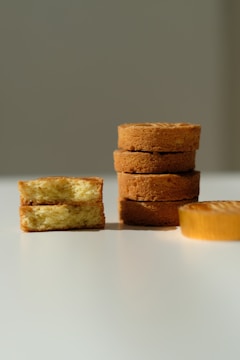 Several slices of cake are arranged on a white surface. On the left, two pieces are stacked with the cake's soft, fluffy interior visible. Toward the right, a stack of four round cakes is neatly aligned, showing their golden-brown crusts.