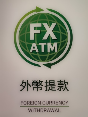 A green and white logo featuring the text 'FX ATM' at the center of a globe with arrows encircling it. Below the logo is text in both Japanese and English that reads 'Foreign Currency Withdrawal'.