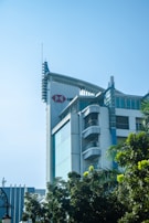 A modern building with a prominent HSBC logo situated near the top, surrounded by lush green trees. The structure features large glass windows and a unique architectural design with vertical elements and a curved facade.