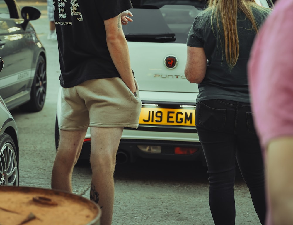 a man and a woman standing in front of a car