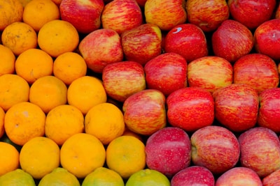 Close-up of ripe, colorful apples and oranges stacked neatly on a rustic table.