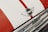 A close-up of a car hood featuring a MINI emblem placed on a white surface with a red stripe running vertically. Below the emblem, there is chrome detailing that adds a reflective, shiny texture.