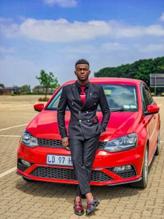 A stylish man in a tailored suit from Lumina Apparel, leaning casually against a classic black car.