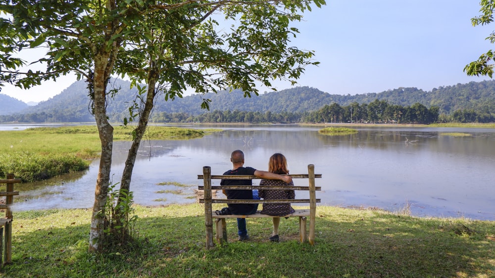 two people sitting on a bench overlooking a lake