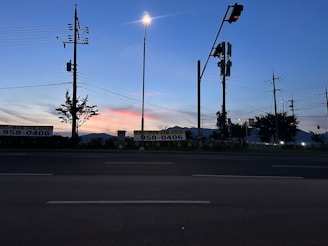 Brightly lit street with electric poles and power lines at dusk.