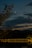 A tranquil night scene features a crescent moon and clouds. In the foreground, there are softly illuminated trees and a body of water reflecting the light from a nearby bridge. In the background, a small, lit structure rests on top of a hill.