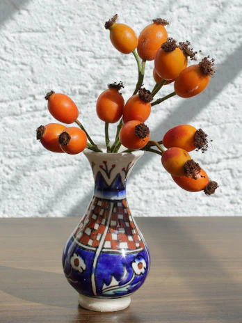 Hand-painted ceramic vase with bold orange and blue patterns on a linen cloth.