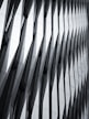 The image features a modern architectural facade with a geometric, repeating pattern of overlapping and protruding panels. The design creates a sense of depth and dynamism, with sharp angles and shadows accentuating the three-dimensional effect.