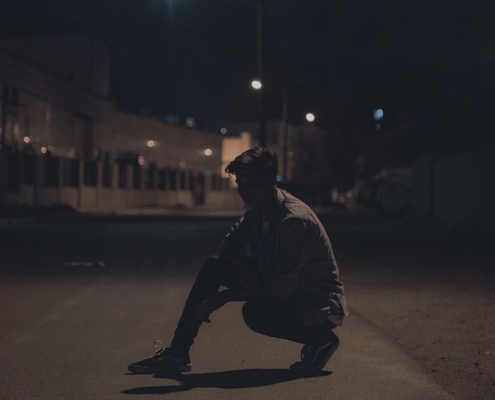 a man squatting down on a street at night