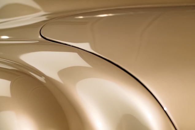 Smooth, flowing curves of a metallic surface with a reflective finish. The image highlights the sleek design and seamless connections with a golden hue.