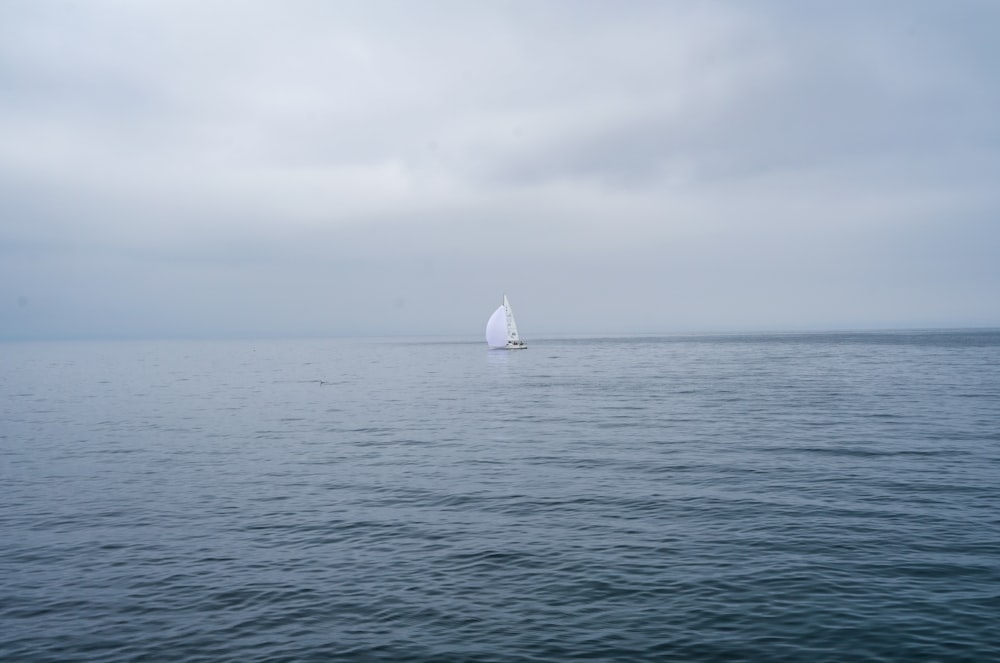 a sailboat in the middle of the ocean on a cloudy day