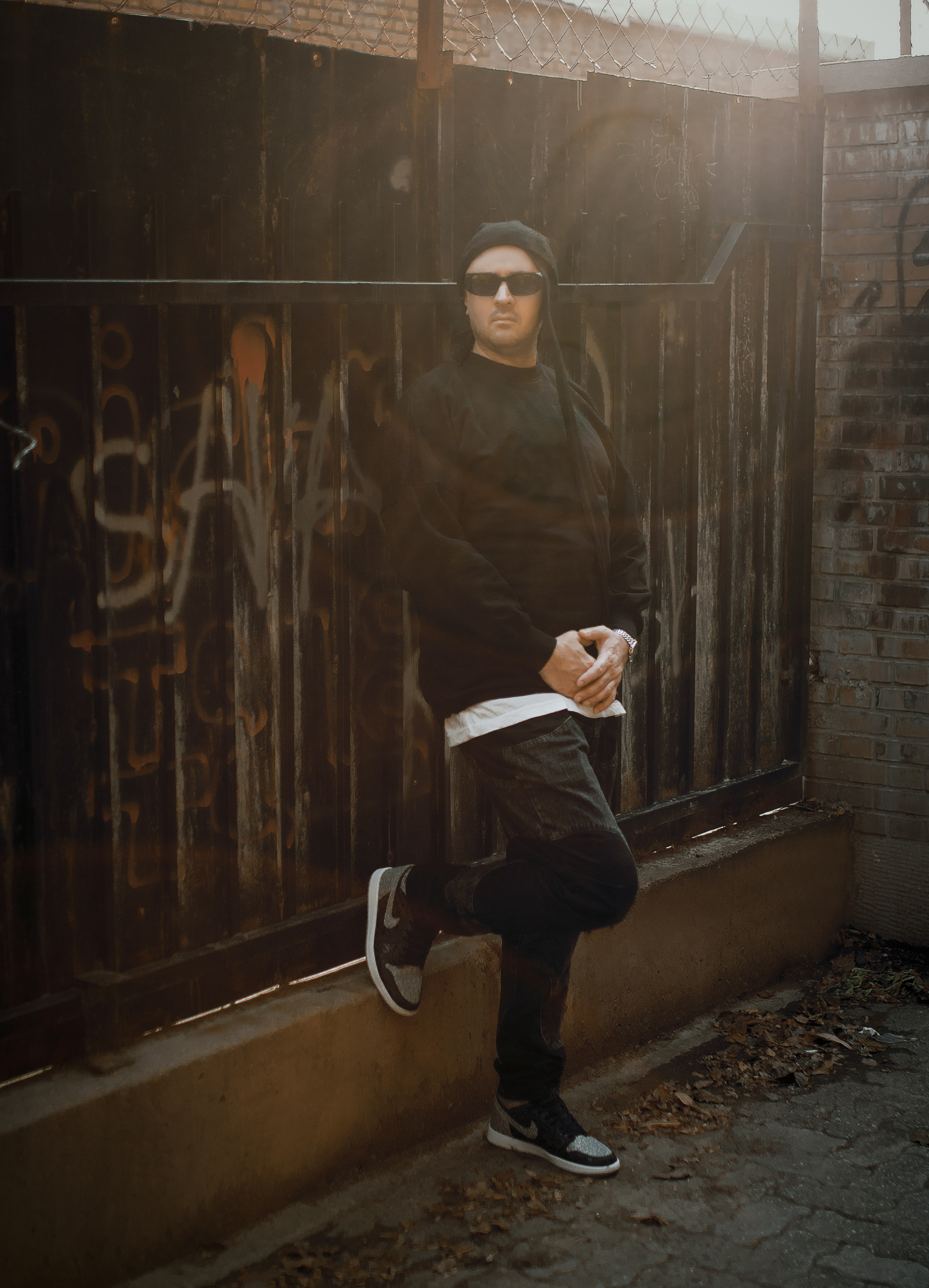 a man in sunglasses leaning against a fence
