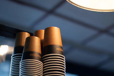 Close-up of a stack of cream white paper cups with subtle leaf patterns and sunlight filtering through.