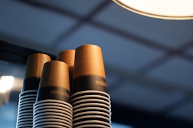 Stacks of paper coffee cups with a brown and black design, arranged against a blurred background with soft lighting.