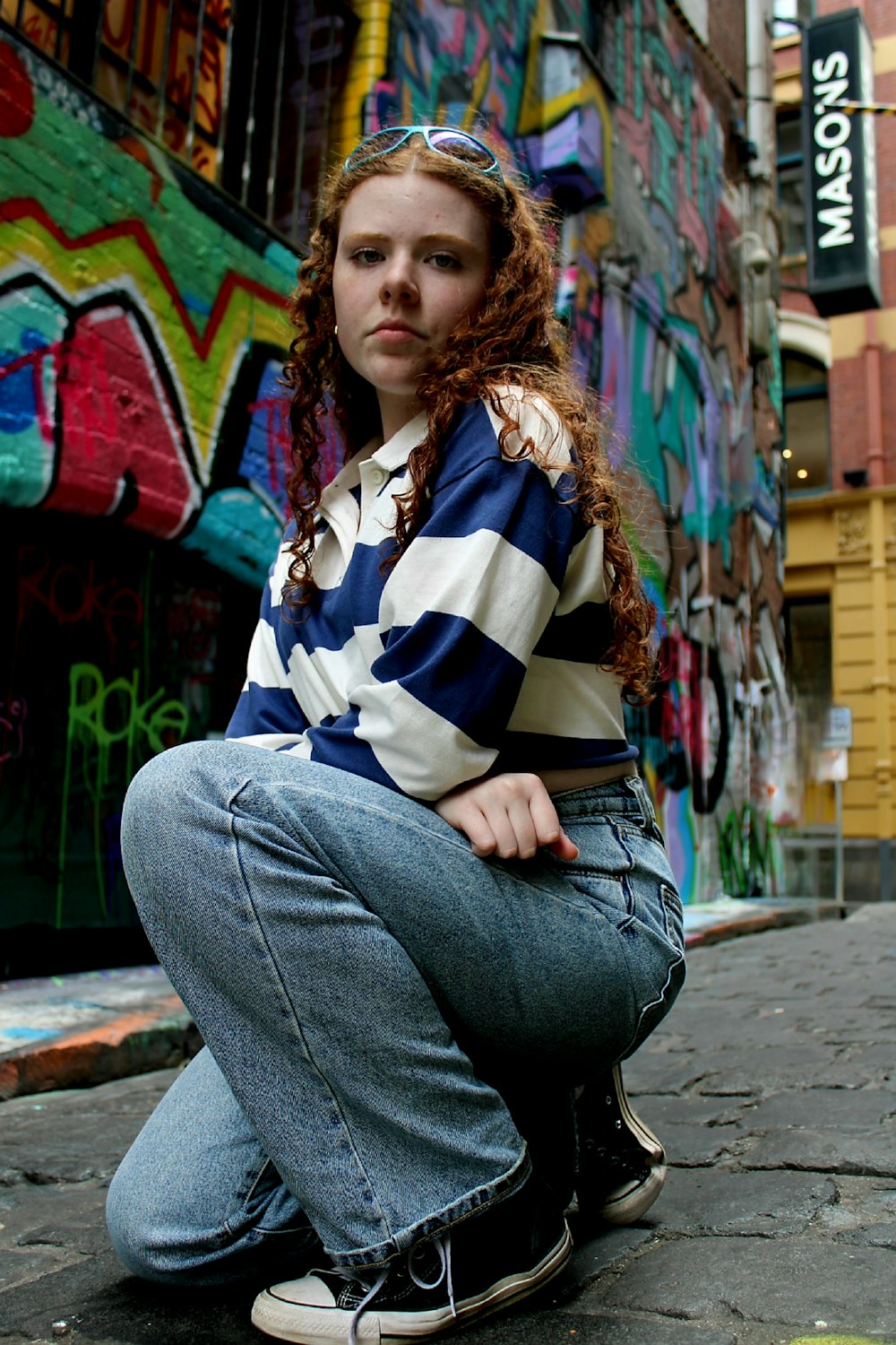 a woman sitting on the ground in front of a wall covered in graffiti